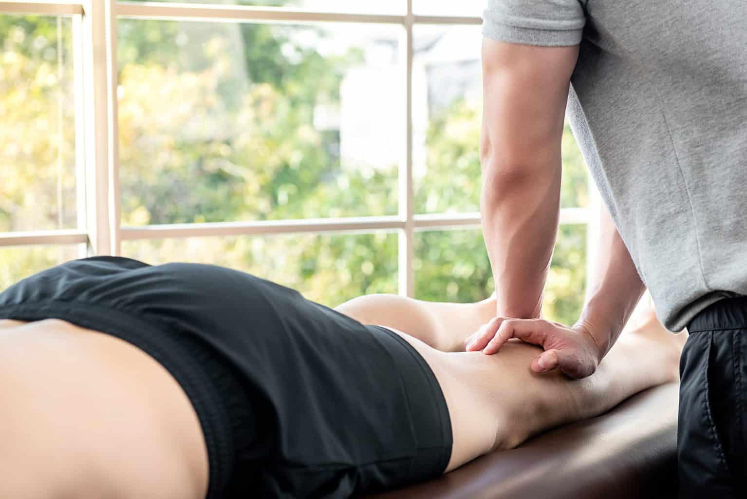 Male therapist giving leg massage to athlete patient in clinic